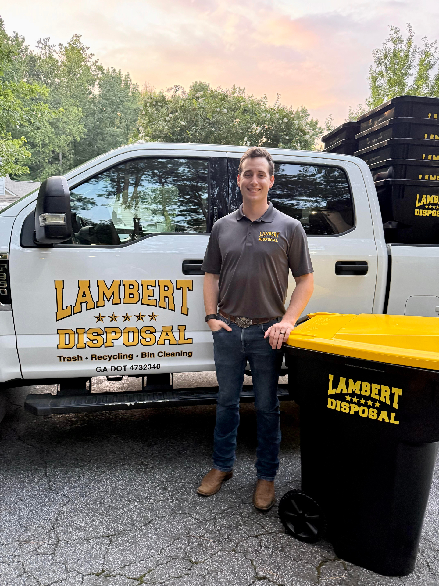 Joseph Lambert standing beside a Lambert Disposal pickup truck at sunset with a Lambert Disposal bin, 2026